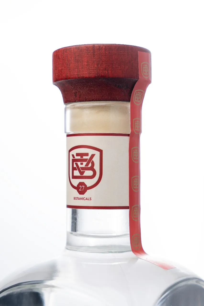 Gargalo da garrafa com a gravata creme, o brasão TB e o selo 27 Botanicals